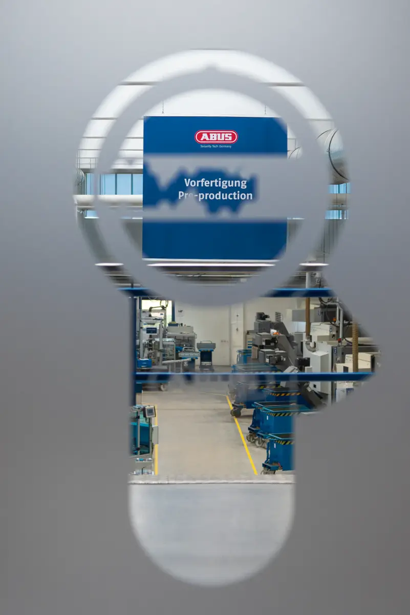 Blick durch ein Fenster in Form eines Schließzylinders auf die Produktion bei ABUS Pfaffenhain